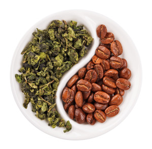 Green leaf tea versus coffee beans in Yin Yang shaped plate, isolated on white